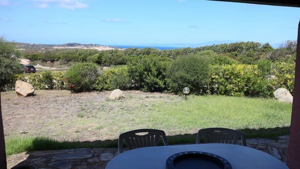 Un espace extérieur abrité, doté d ’une table et de chaises, qui offre une vue sur un paysage naturel avec des arbres et une perspective lointaine sur la mer.