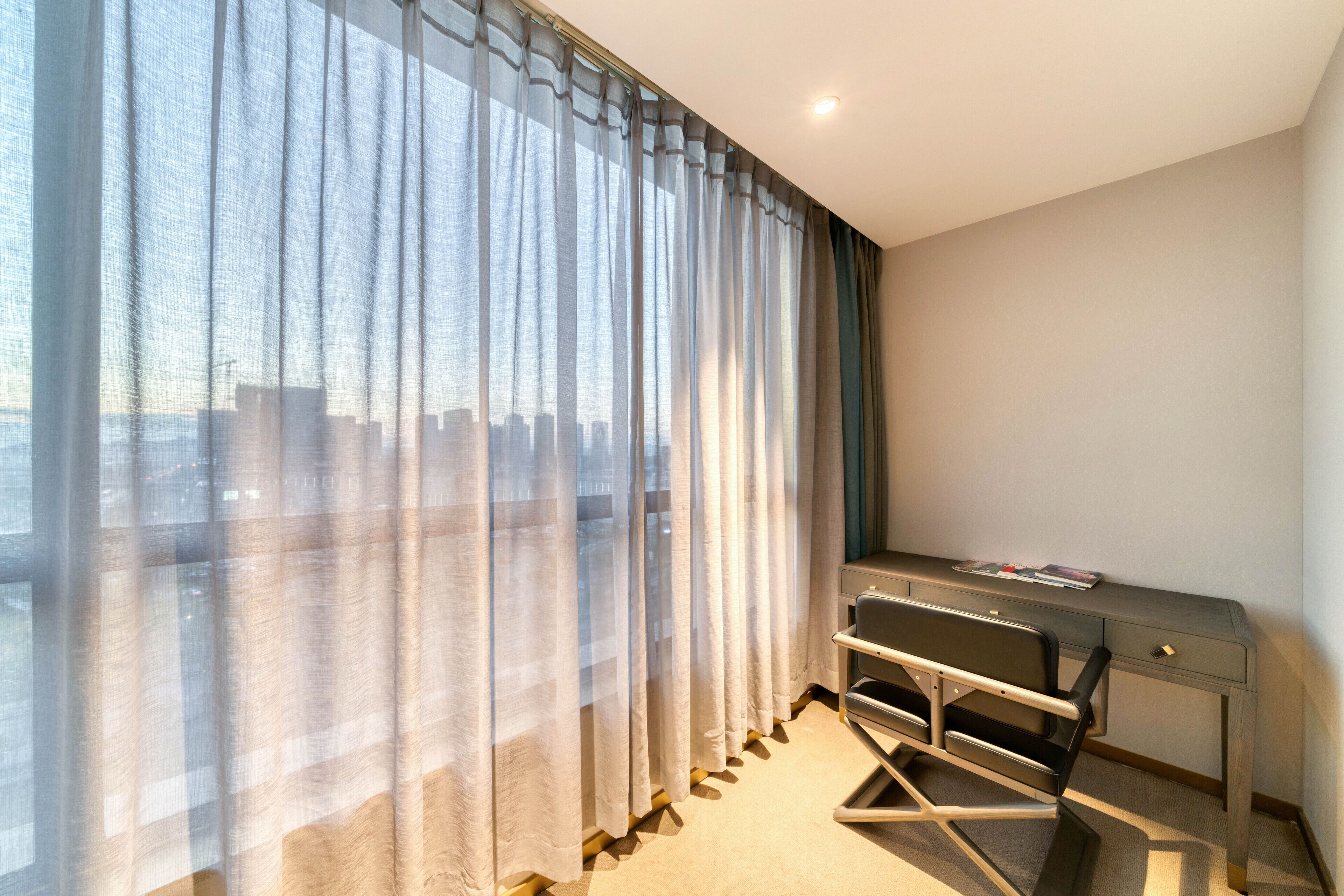 A hotel room with a large window, a desk, and a chair.