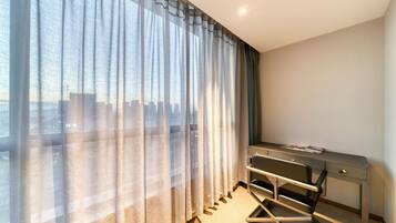 A hotel room with a large window, a desk, and a chair.