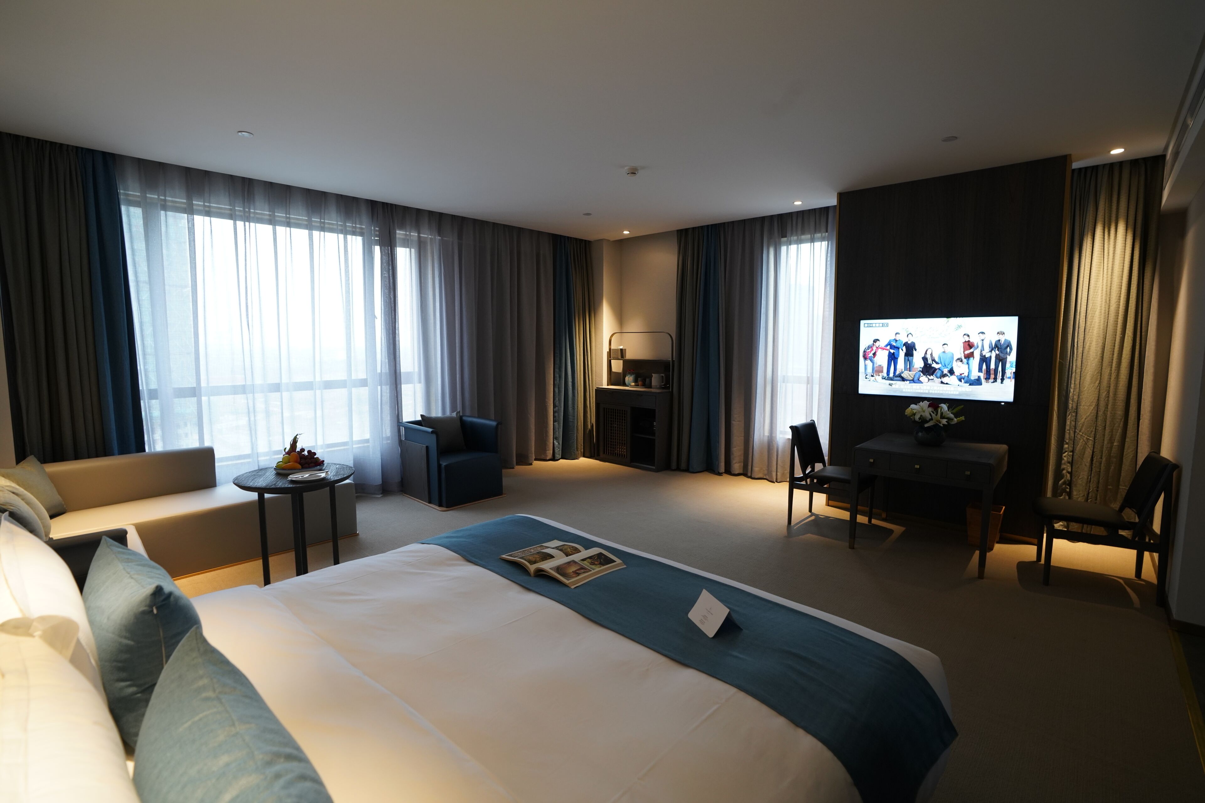 A modern hotel room with a large bed, a sofa, a desk, and a television.