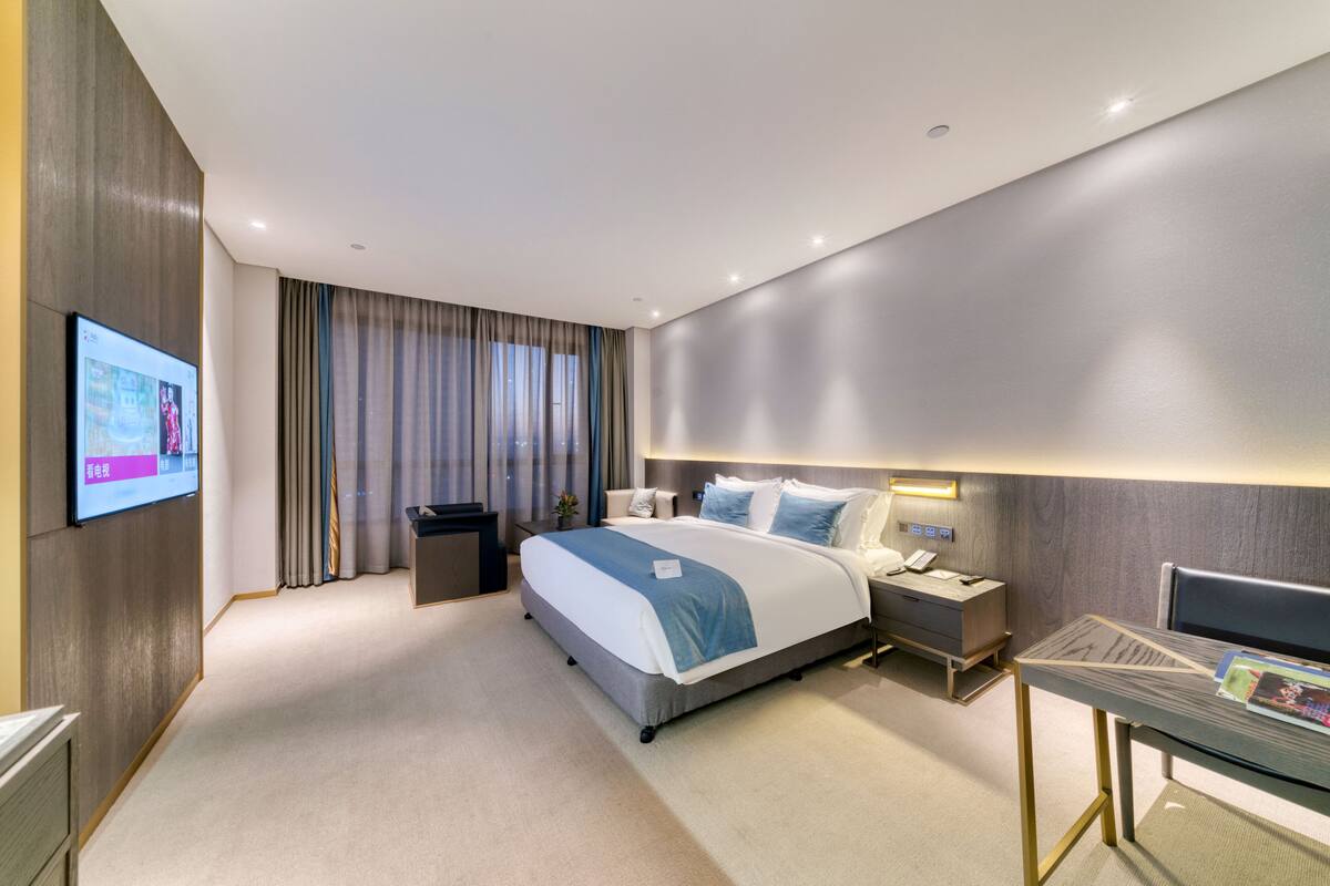A modern hotel room with a large bed, bedside tables, a desk, and a TV mounted on the wall.