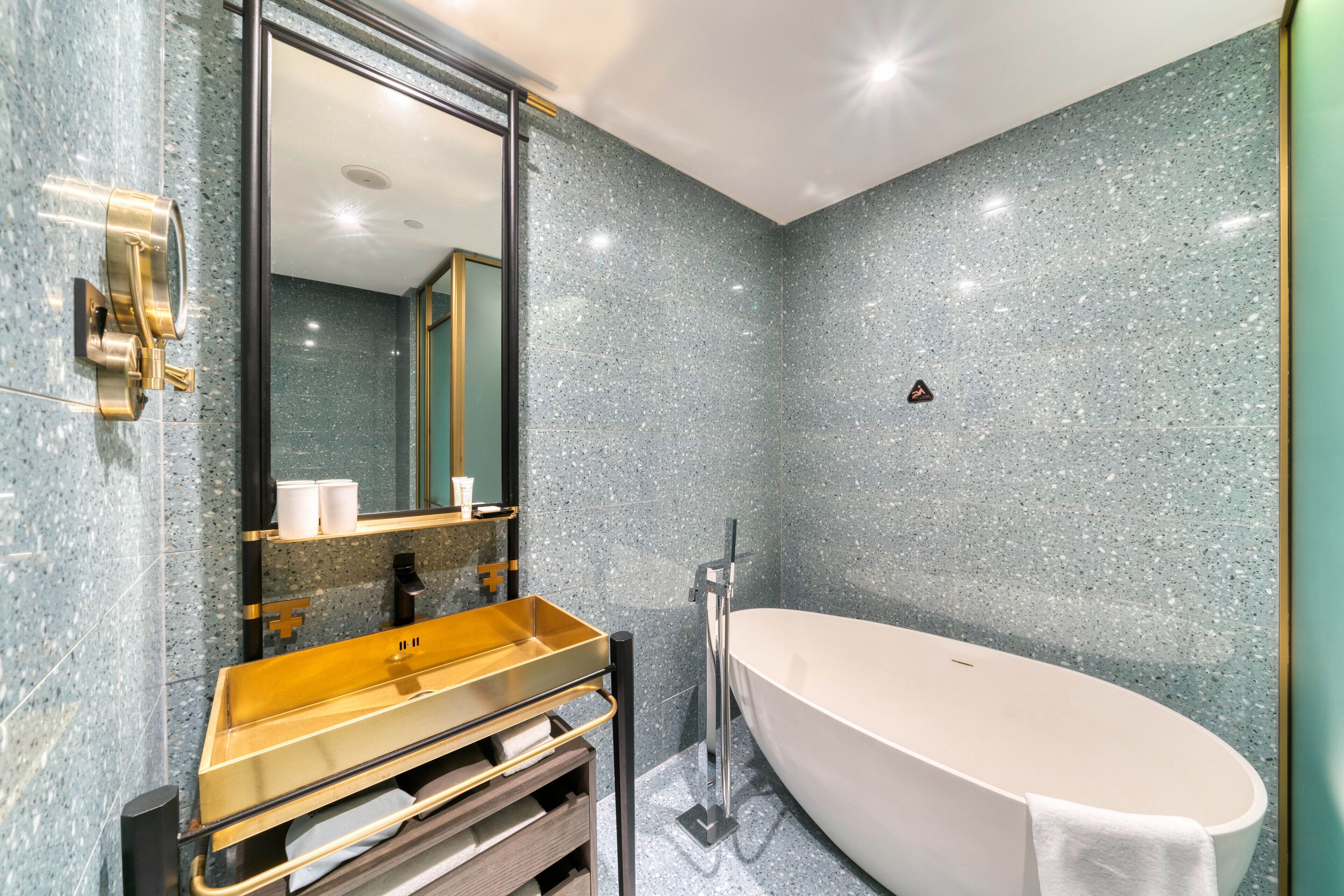 Un baño moderno con una bañera independiente, un tocador dorado y un espejo grande.