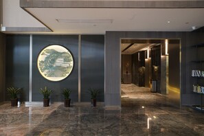 Un vestíbulo moderno con una obra de arte circular, plantas en macetas y un suelo de mármol.