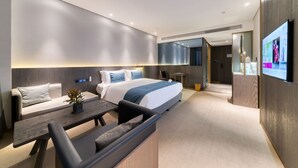 Una habitación de hotel moderna con una cama grande, un sofá, un escritorio y un televisor montado en la pared.