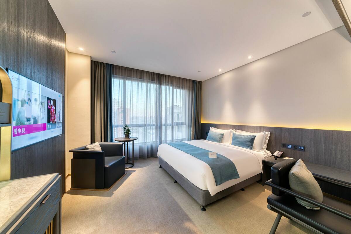 A modern hotel room with a large bed, a desk, a TV, and a seating area.