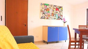 A room with a bed, a blue cabinet, a dining table with chairs, and a colorful artwork on the wall. - Le Perle del Centro (Santa Teresa di Gallura)