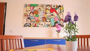 A dining area with a table, chairs, a colorful artwork on the wall, and a potted plant. - Le Perle del Centro (Santa Teresa di Gallura)