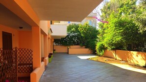 A covered outdoor area with a tiled floor, orange walls, and potted plants. - Le Perle del Centro (Santa Teresa di Gallura)