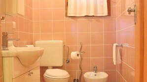 A small bathroom with a toilet, bidet, sink, and a window with a curtain. - Casa di Anna (Santa Teresa di Gallura)