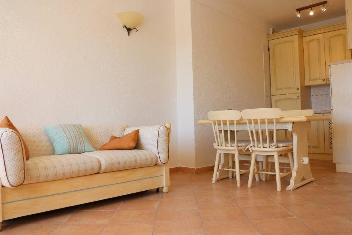 A living room with a sofa, two chairs, a small table, and a kitchen area with cabinets and a refrigerator.