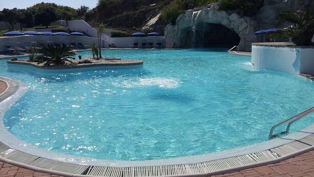 Ein klares, blaues Schwimmbecken mit felsigem Hintergrund, Liegestühlen und Sonnenschirmen.