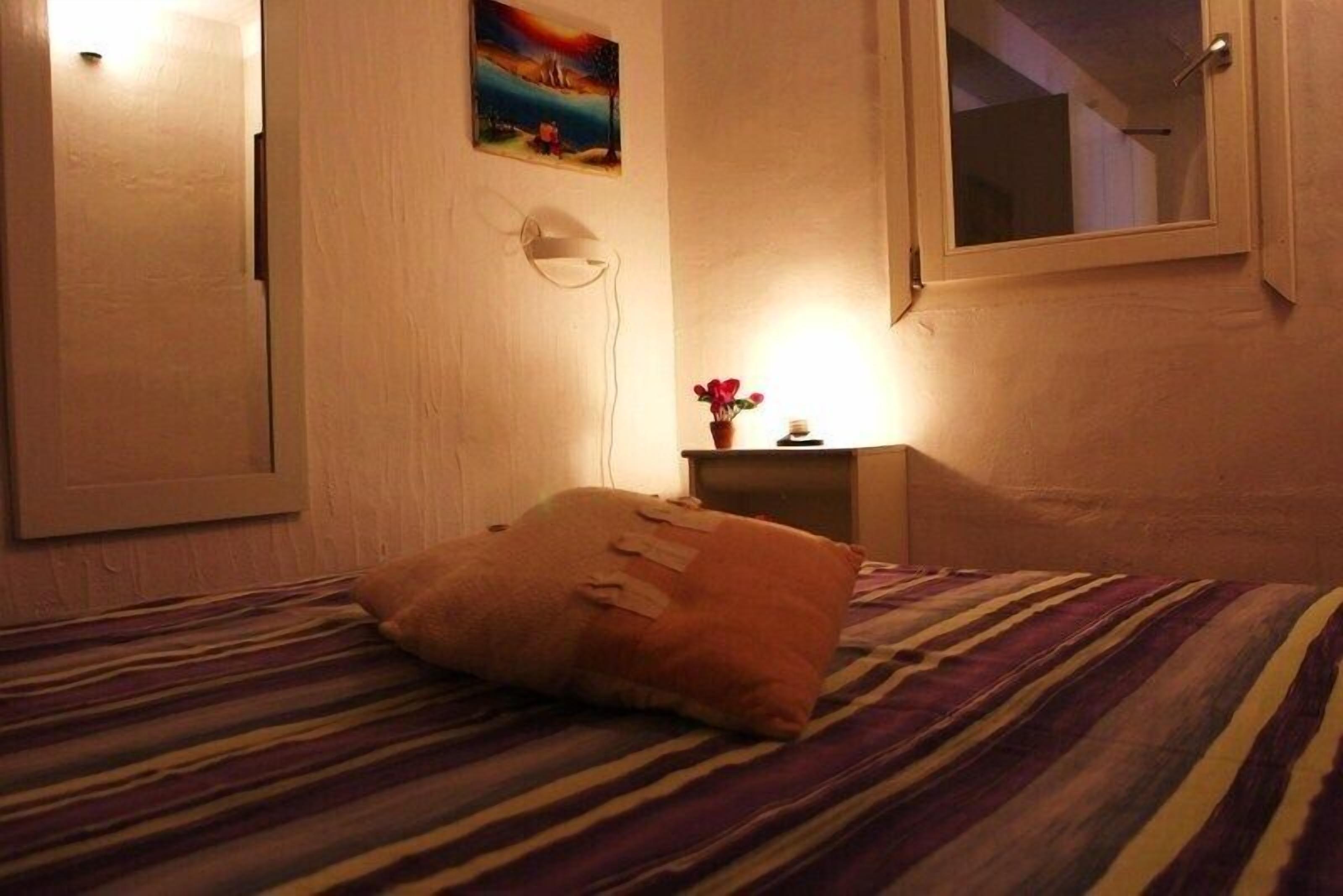 Una habitación de hotel con una cama, una mesita de noche con lámpara, un cuadro en la pared y una ventana.