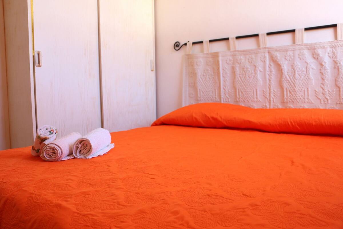 A neatly made bed with rolled towels and an orange bedspread.