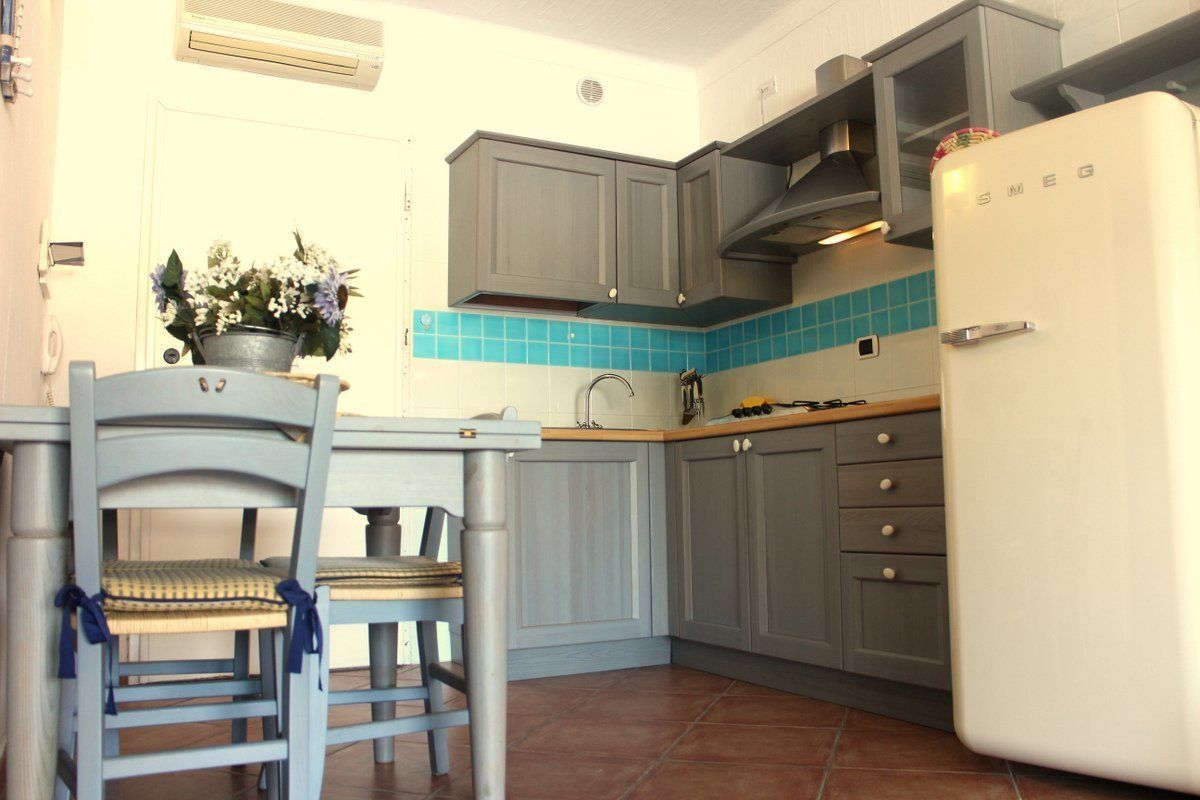 Una cocina con gabinetes grises, un refrigerador blanco y un salpicadero de azulejos azules.