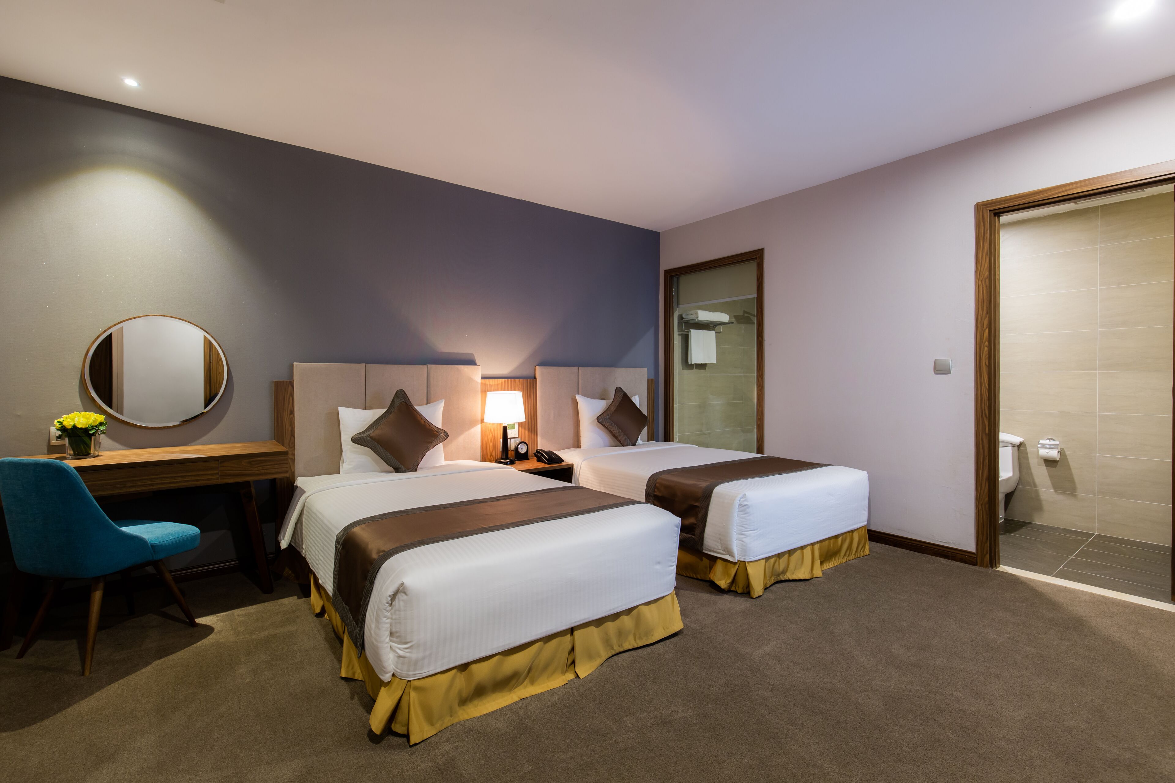 Hotelkamer met twee bedden, een bureau met stoel, een ronde spiegel en een badkamer met toilet en douche.