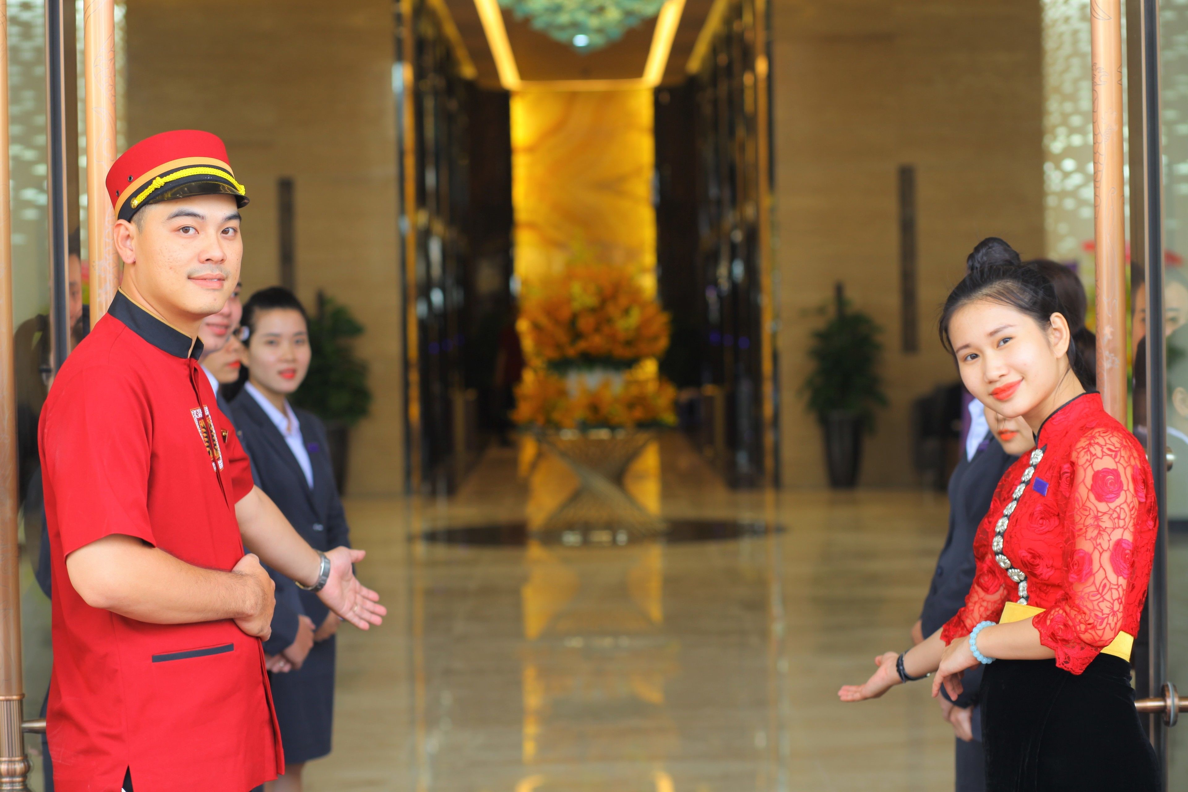 A hotel lobby with a polished floor, a reception desk, and a floral arrangement in the background.