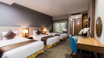 A hotel room with three beds, a wooden desk, a blue chair, and a mirror.