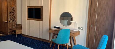 A hotel room with a bed, a desk with a chair, a TV, a mirror, and a wardrobe.
