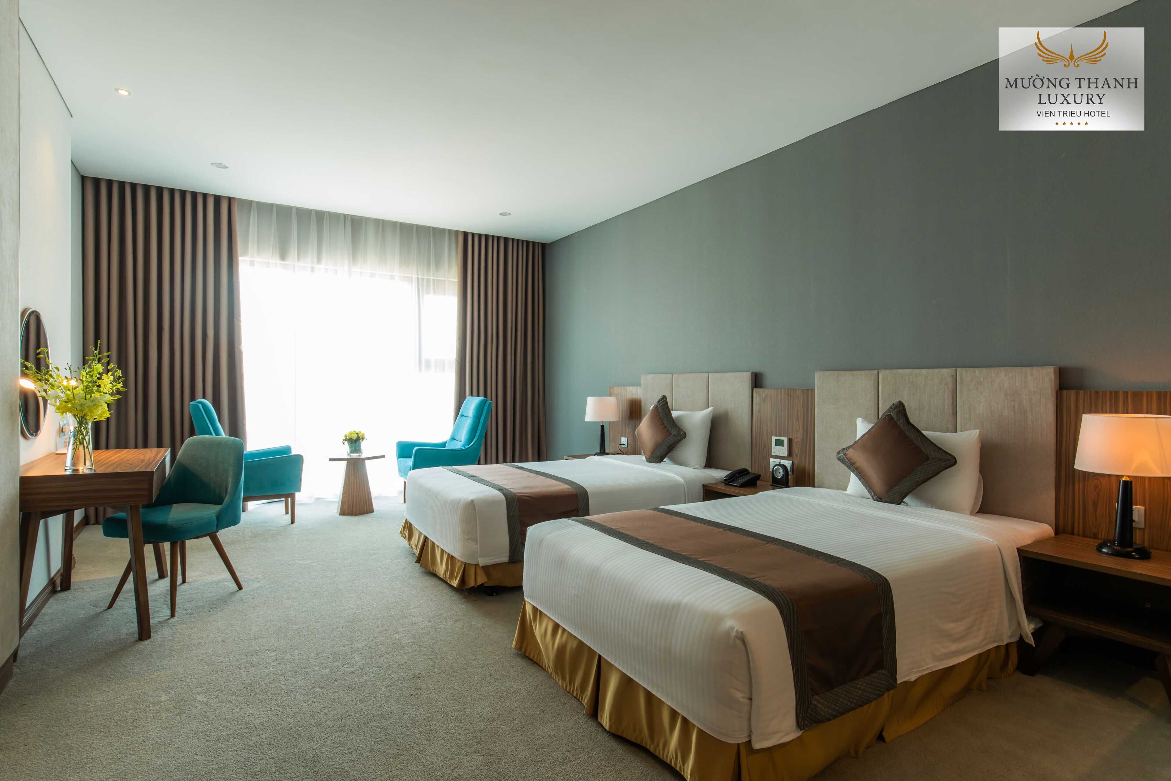 Habitación de hotel con dos camas, un escritorio, una silla y una lámpara.