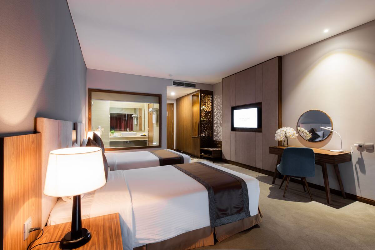 Une chambre d’hôtel avec deux lits, un bureau, une chaise, une télévision et un miroir.
