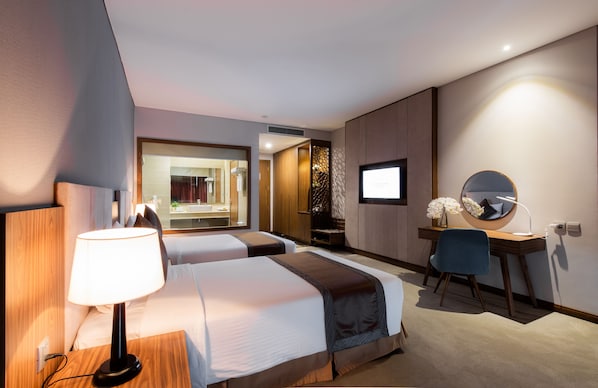Ein Hotelzimmer mit zwei Betten, einem Schreibtisch, einem Sessel, einem Fernseher und einem Spiegel.