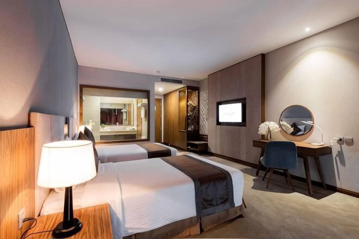 Une chambre d’hôtel avec deux lits, un bureau, une chaise, une télévision et un miroir.