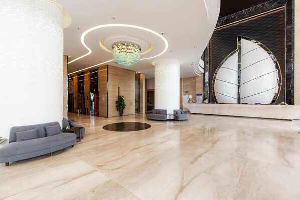 A spacious lobby with a modern design, featuring a large reception desk, seating area, and a decorative chandelier.