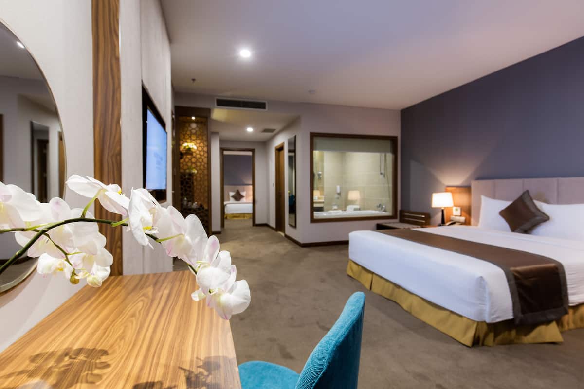 Une chambre d’hôtel avec un lit, un bureau et une télévision. On aperçoit une salle de bain au fond.