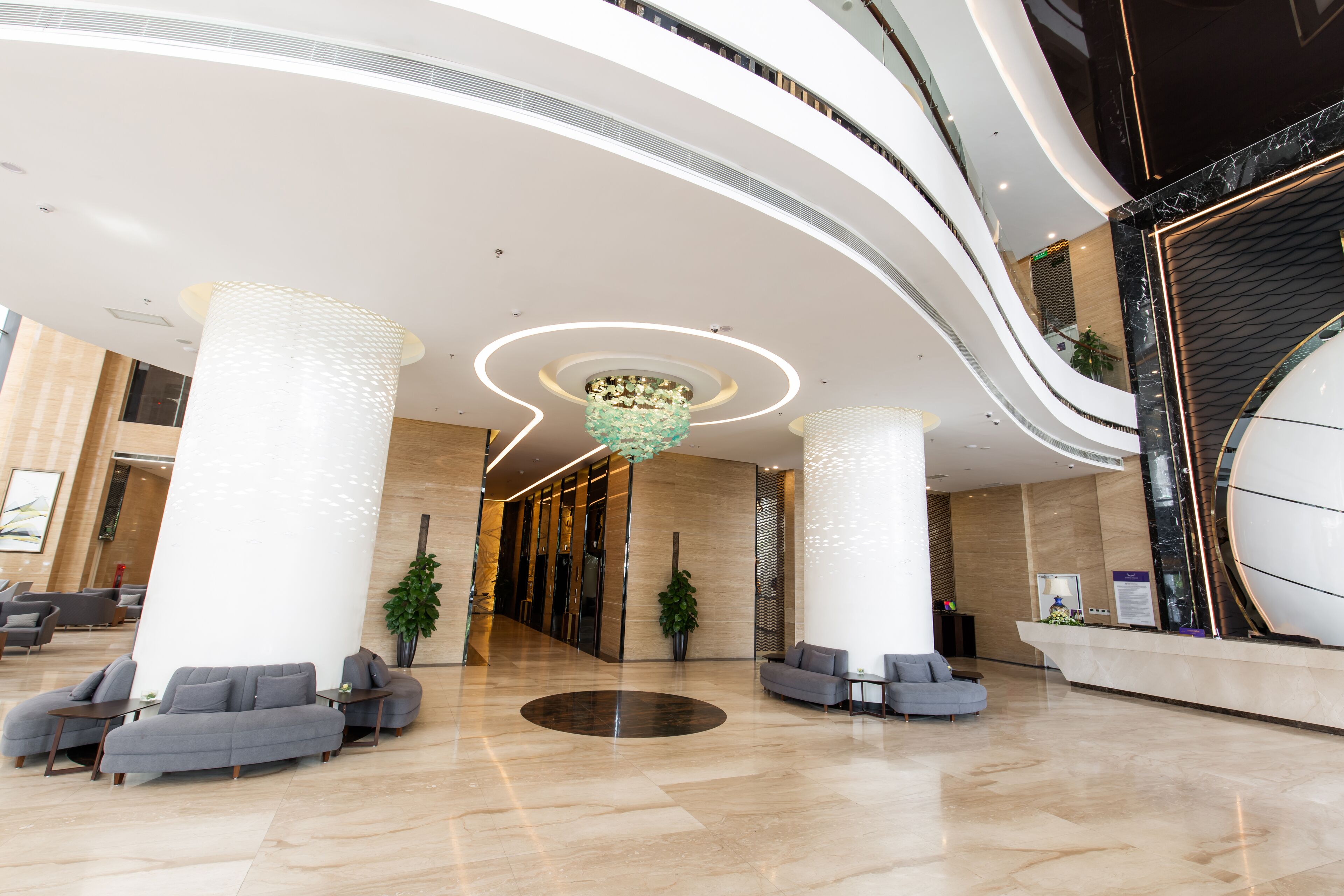 A spacious lobby with a central circular seating area, large white pillars, and a modern chandelier.