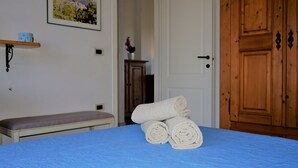 A bedroom with a blue bedspread, a wooden door, a bench, and a framed picture on the wall. - Residence Lampara (Santa Teresa di Gallura)