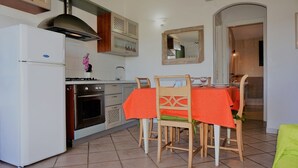 A compact kitchen with a refrigerator, stove, oven, and a dining table with chairs. - Residence Lampara (Santa Teresa di Gallura)