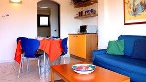 A living room with a blue sofa, a wooden coffee table, and a dining area with a red tablecloth and blue chairs. - Residence Lampara (Santa Teresa di Gallura)