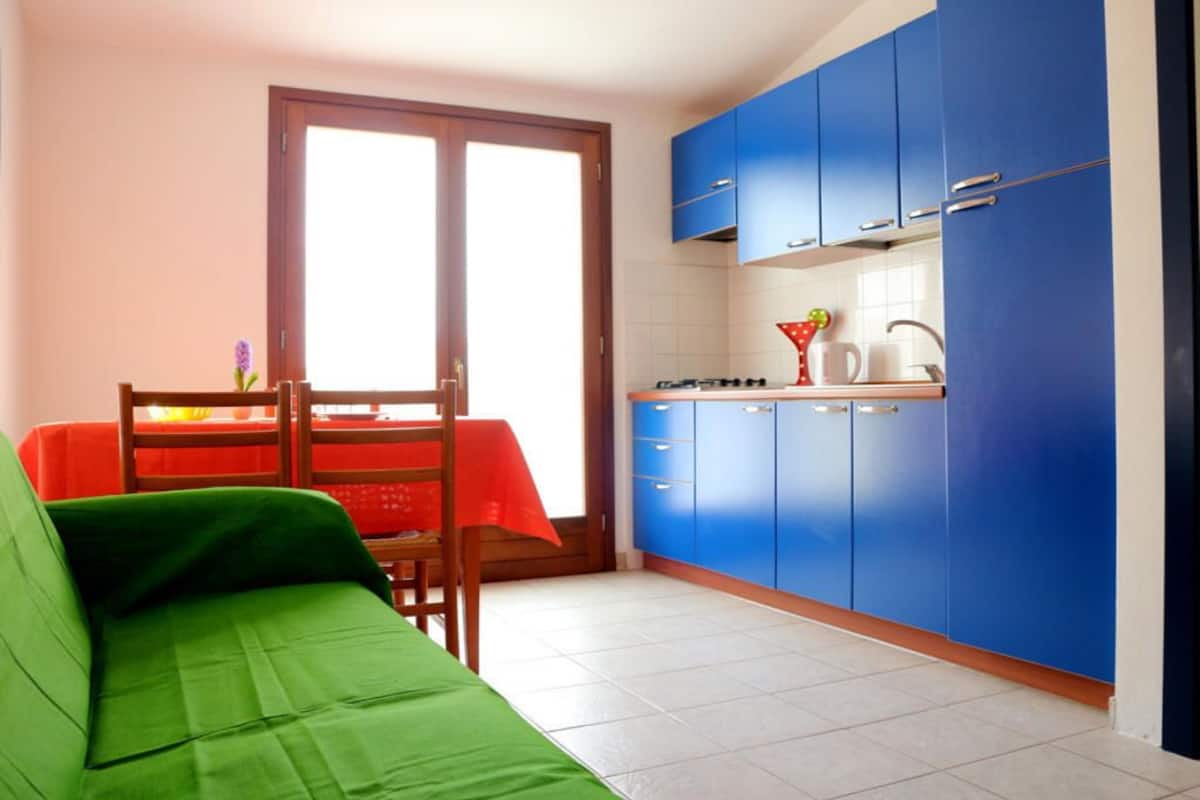 A compact kitchen with blue cabinets, a dining table with a red tablecloth, and a green sofa.