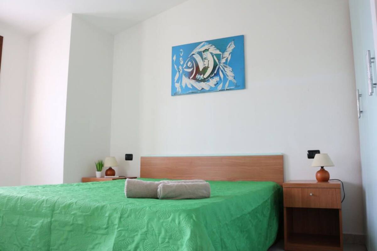 A neatly made bed with a green bedspread, a wooden headboard, and a wall-mounted painting.