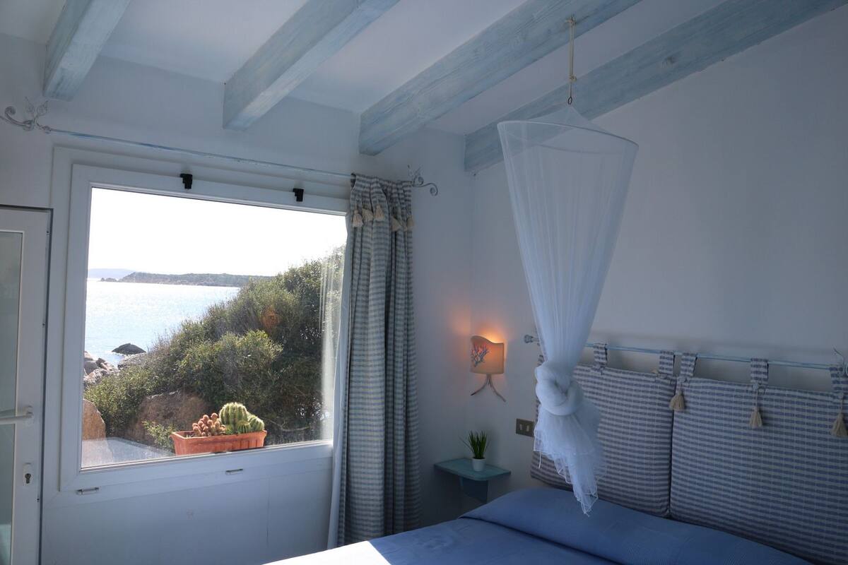 Une chambre avec une grande fenêtre, un lit, une table de chevet avec une lampe et un baldaquin.