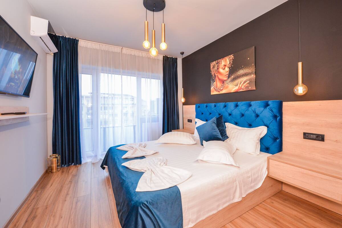 A modern hotel room with a large bed, a TV, and a painting on the wall.