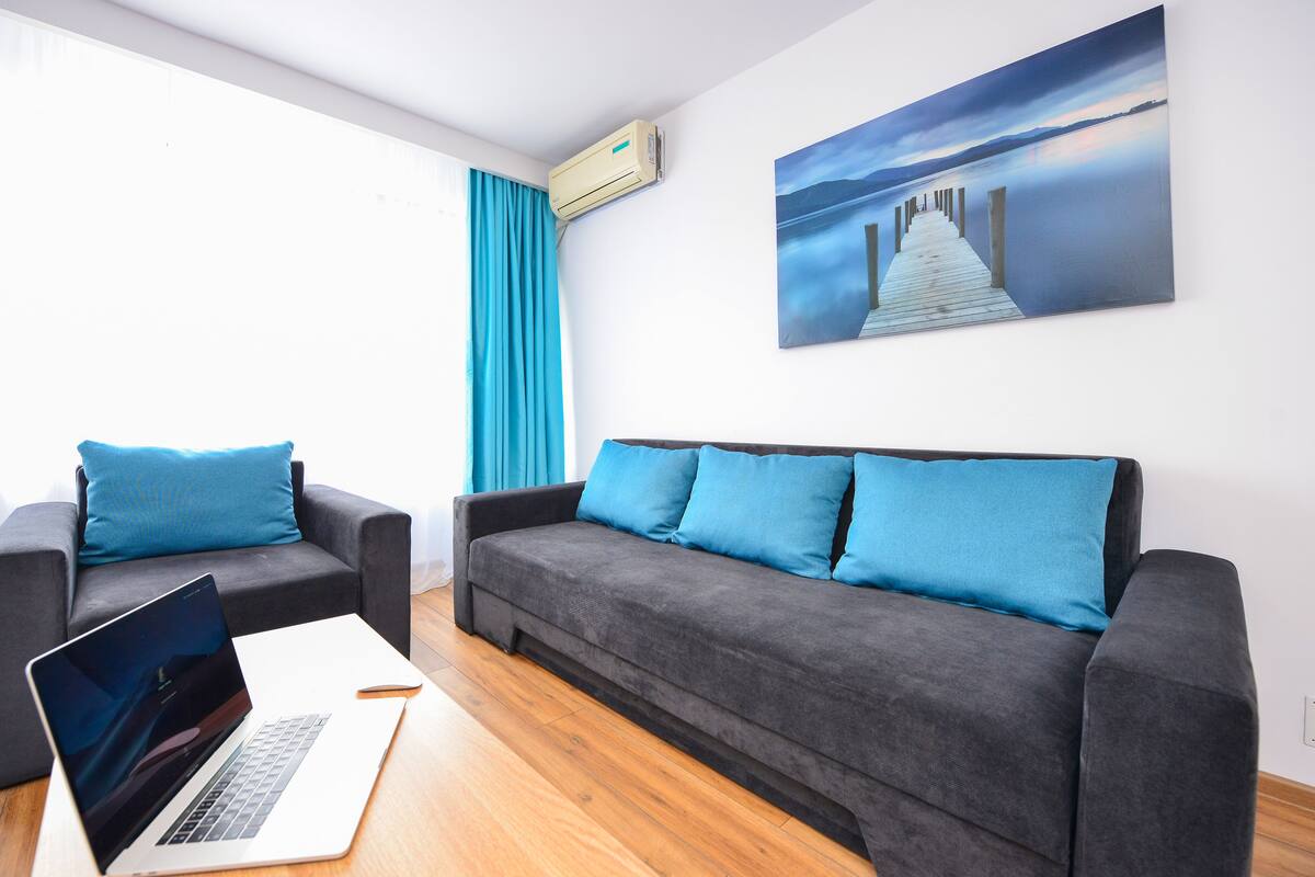 A modern living room with a grey sofa, a blue couch, and a wooden floor.