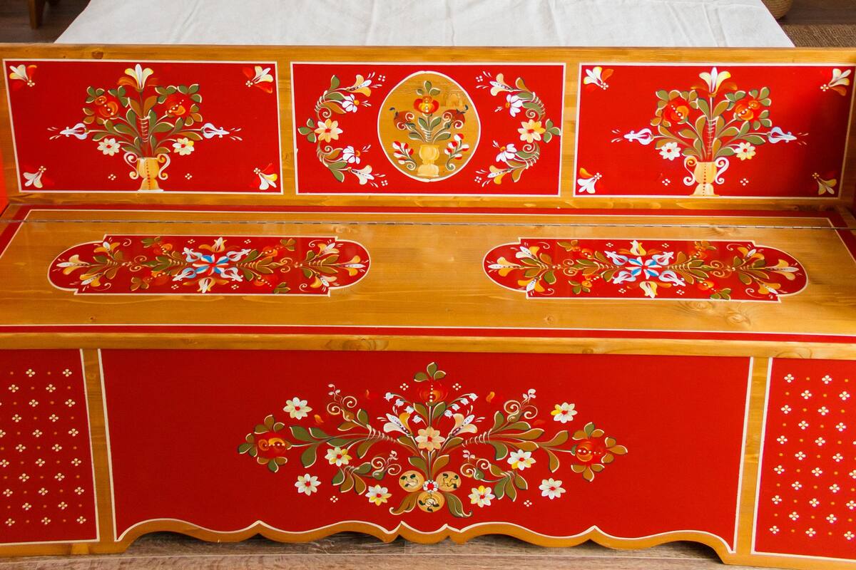 A neatly made bed with a red and gold headboard, a bedside table with a lamp, and three framed artworks on the wall.