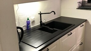 Ett kök med vita skåp, en svart bänkskiva och en svart diskho.