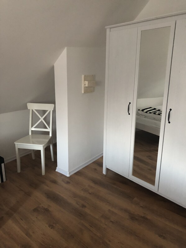 A room with a white wardrobe, a white chair, and a bed with a striped pillow. - Ilmhaus 2 (Pförring)
