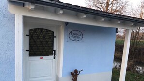 En byggnadsentré med en blå fasad, en vit dörr med ett metallgaller, en liten änglastaty och en skylt med texten "Almhaus Gaden".