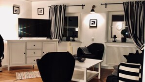 Ett modernt vardagsrum med en platt-TV, ett matbord och en svart soffa.