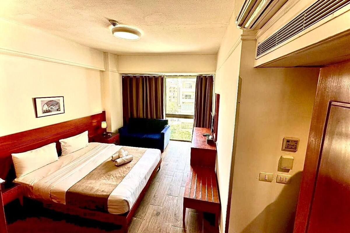A hotel room with a bed, a desk, a chair, a window with curtains, and a door.