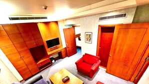 Een woonkamer met een bank, fauteuils, een salontafel, een televisie en houten kasten.