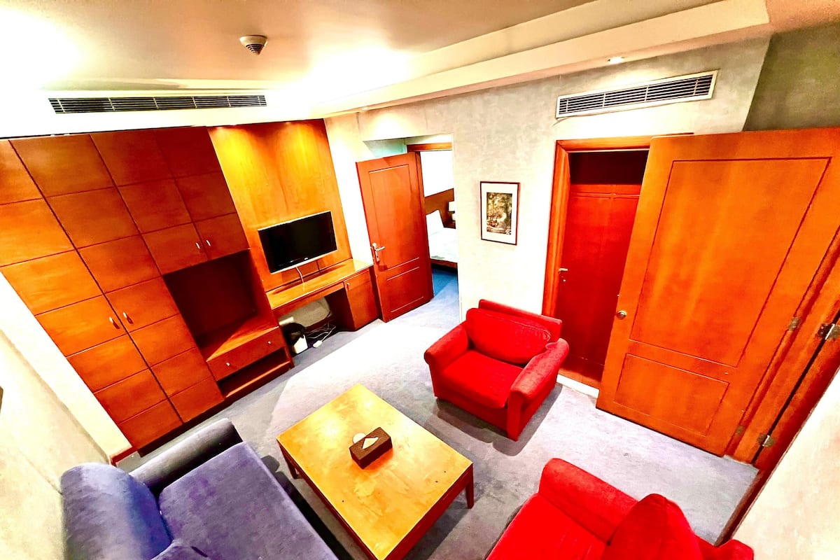 A living room with a sofa, armchairs, a coffee table, a TV, and wooden cabinets.