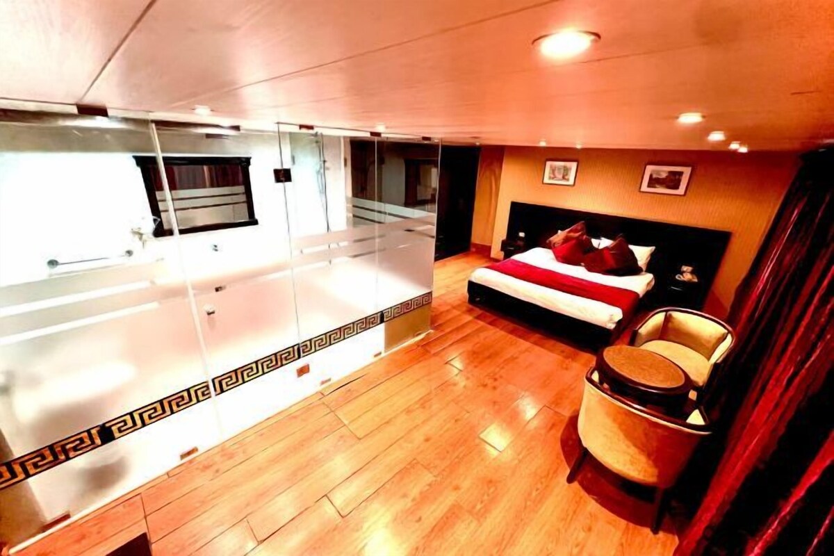 A hotel room with a large mirror, a bed with red bedding, a chair, and a wooden floor.