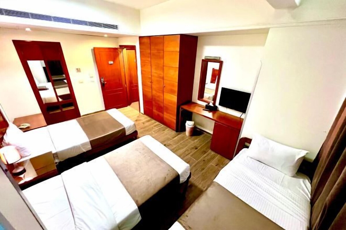 A hotel room with two single beds, a desk with a TV, a wardrobe, and a mirror.