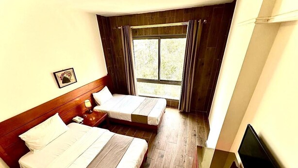 Een hotelkamer met twee bedden, een televisie en een raam met gordijnen.