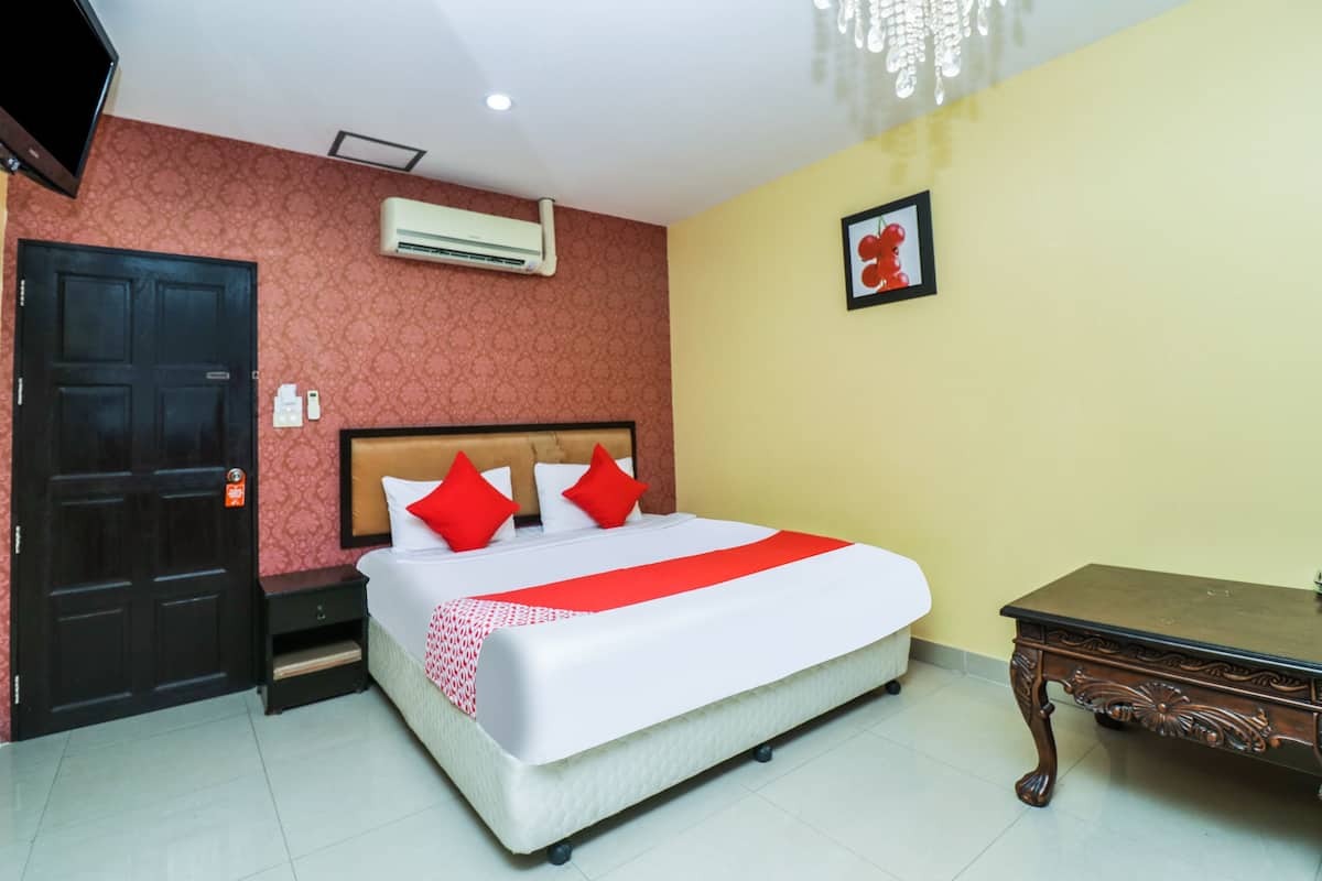 A hotel room with a bed, a nightstand, a wooden table, a TV, and an air conditioning unit.