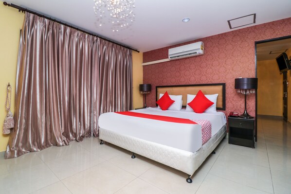 A hotel room with a large bed, a nightstand, an air conditioning unit, and a curtain. - OYO 131 Griebs Inn (Pattaya)